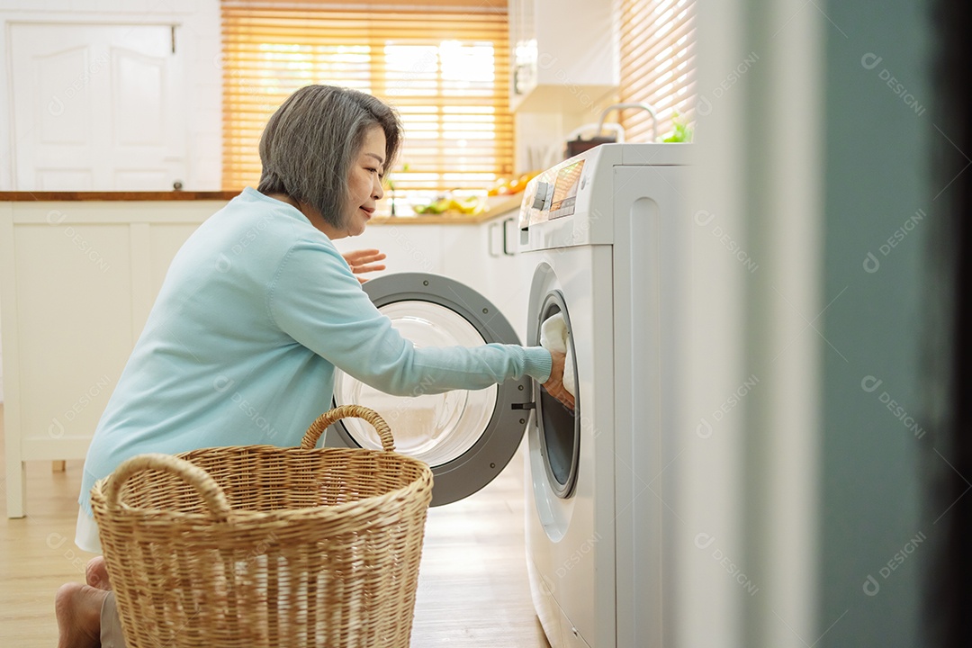 Mulher sênior asiática carregando roupas para a máquina de lavar.