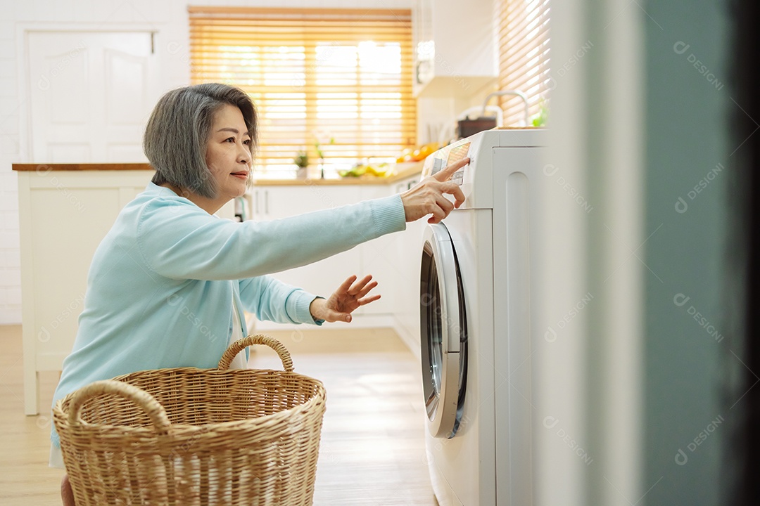 Mulher sênior asiática carregando roupas para a máquina de lavar.