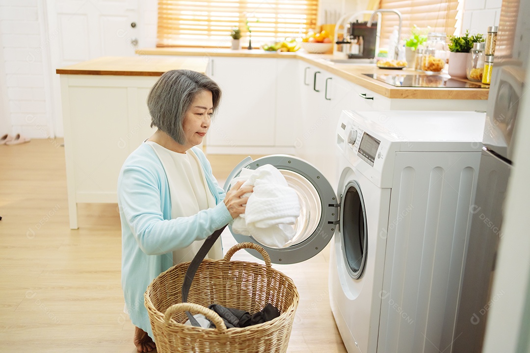 Mulher sênior asiática carregando roupas para a máquina de lavar.