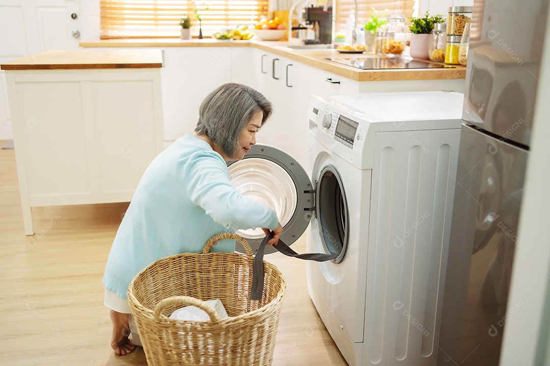 Mulher sênior asiática carregando roupas para a máquina de lavar.