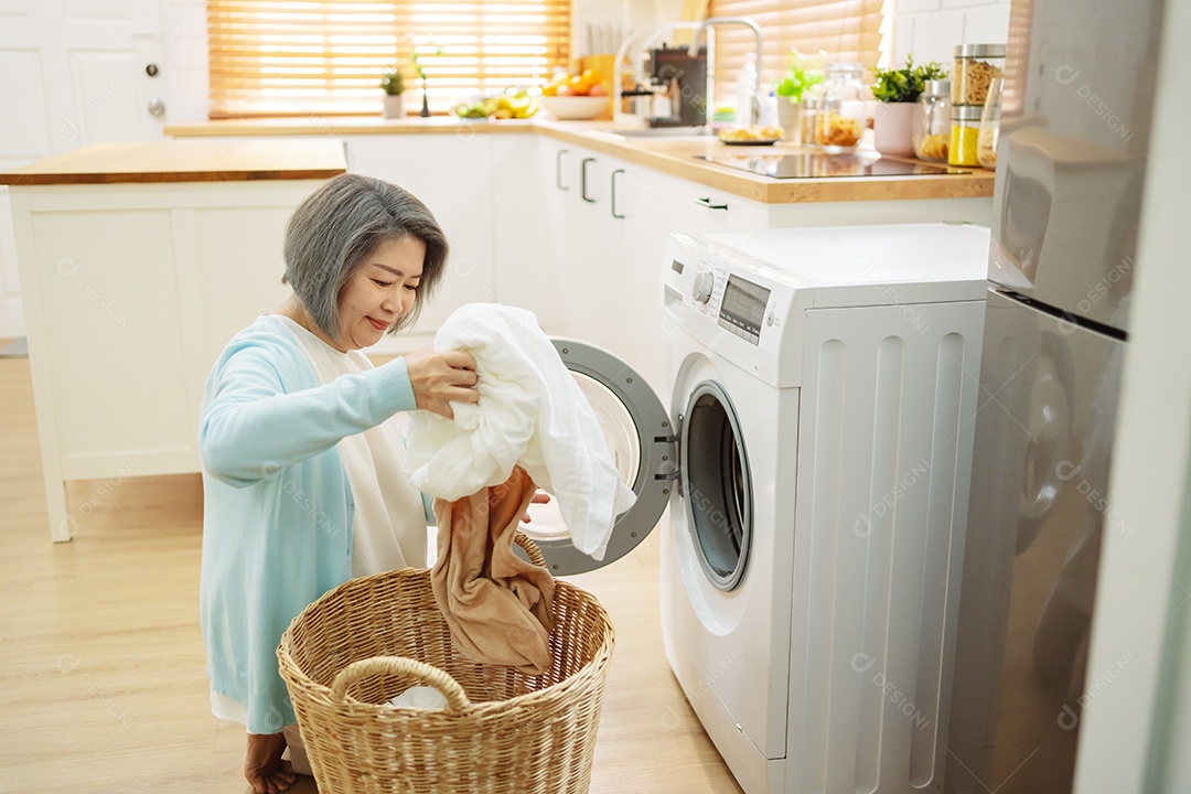 Mulher sênior asiática carregando roupas para a máquina de lavar.