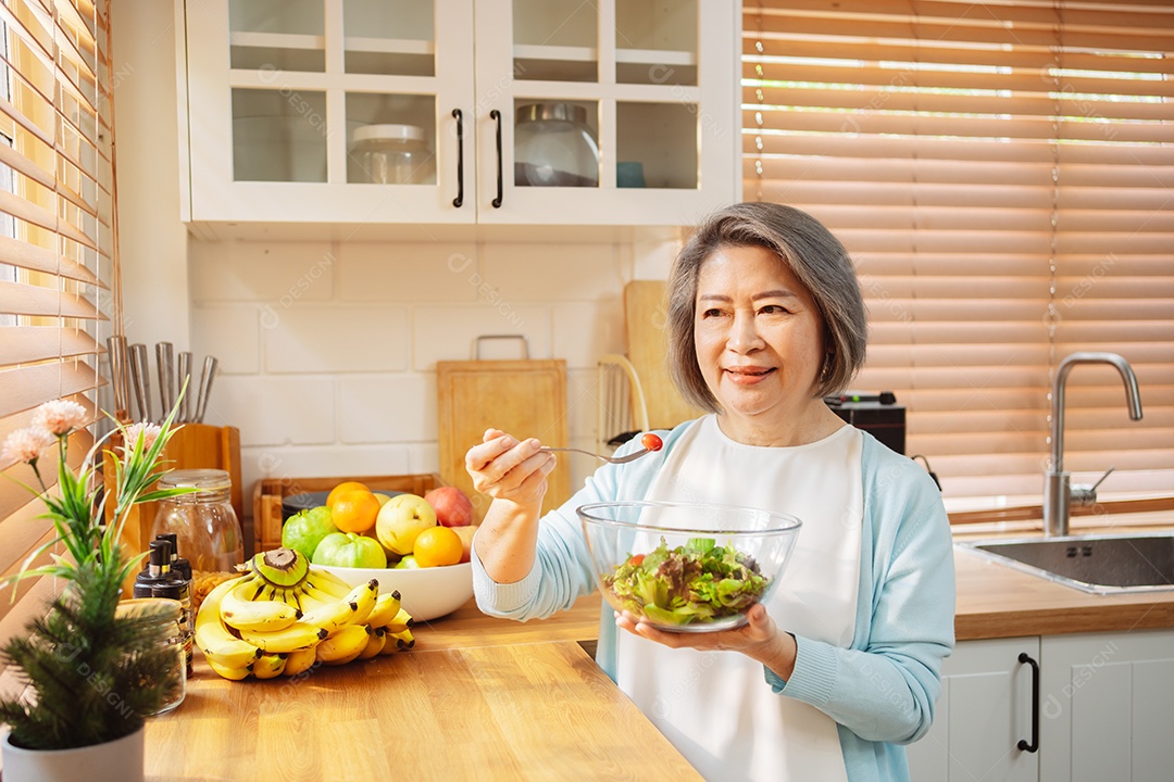 Mulher sênior asiática feliz comendo comida limpa para uma alimentação saudável na cozinha