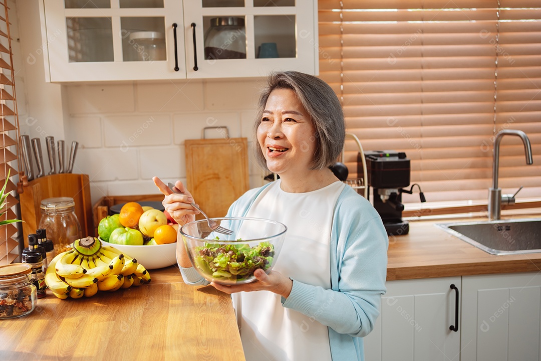 Mulher sênior asiática feliz comendo comida limpa para uma alimentação saudável na cozinha