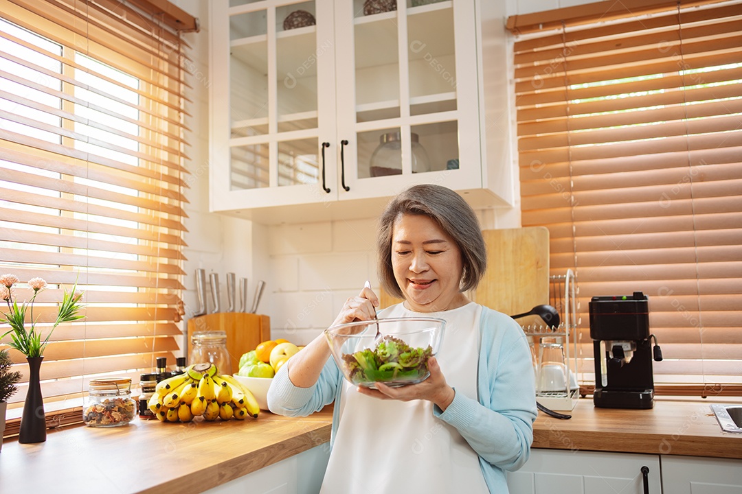 Mulher sênior asiática feliz comendo comida limpa para uma alimentação saudável na cozinha