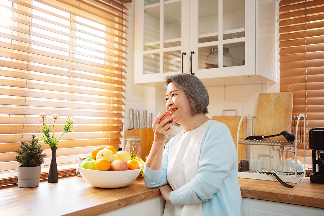 Mulher sênior asiática feliz comendo comida limpa para uma alimentação saudável na cozinha