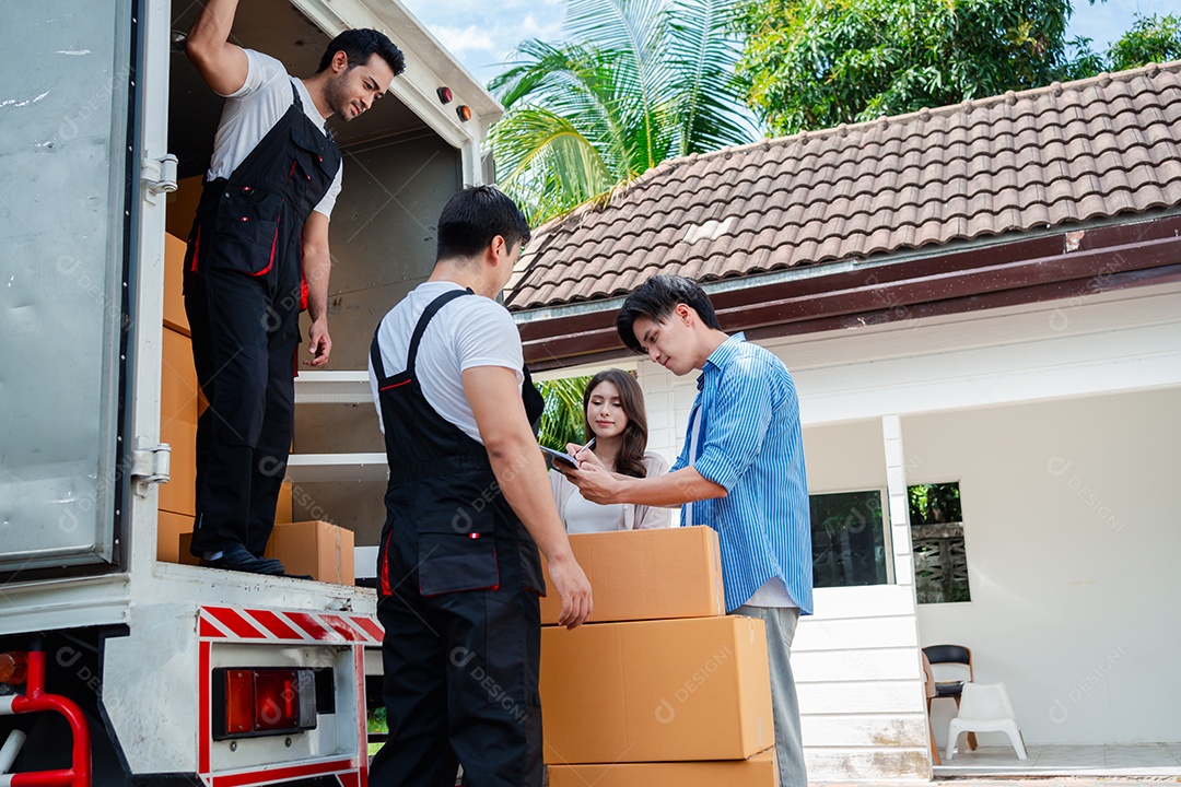 Verificação de casal asiático ao descarregar caixas e móveis de uma caminhonete para uma nova casa