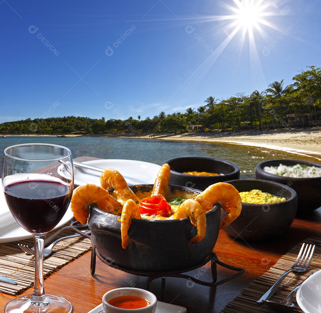 Moqueca de creme de camarão com guarnições e taça de vinho