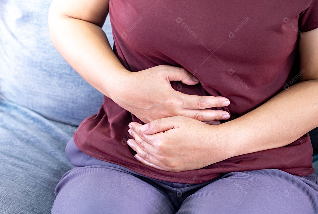 Mulher gorda com dor de estômago. comer na hora por querer controlar o peso no sofá da sala, Gastrite crônica.