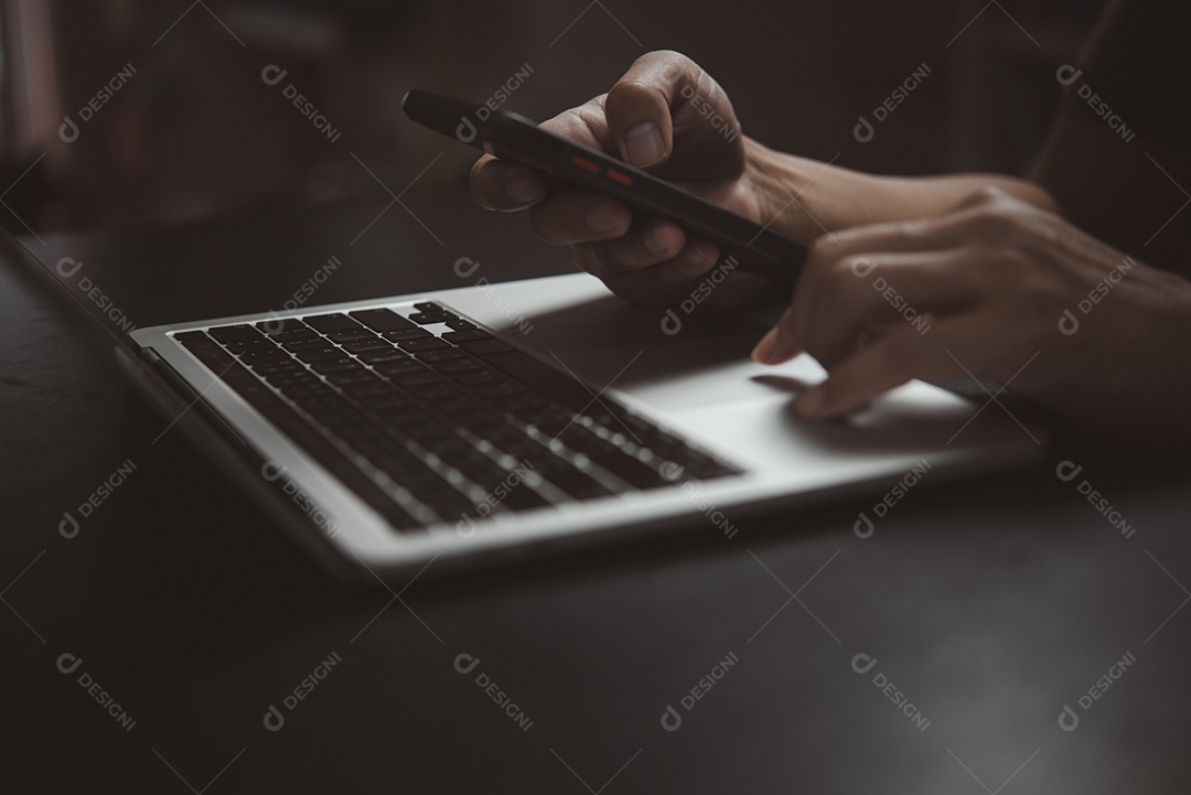 homem usando o telefone inteligente móvel de busca de informações e trabalhando na computação do laptop.