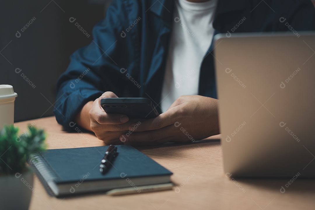 homem usando telefone inteligente móvel e trabalhando em laptop computer.