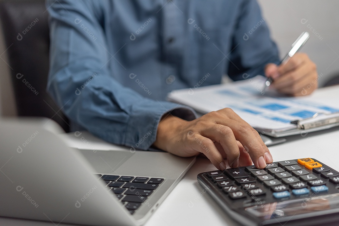 Empresário usando calculadora e documentos contábeis na mesa com computador portátil.