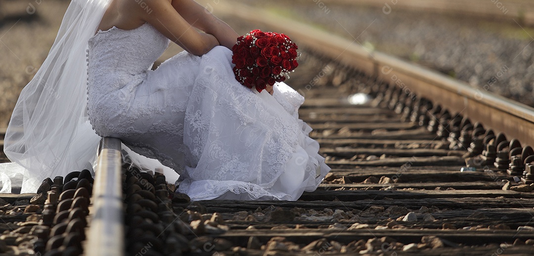Noiva sentada em um trilho com buquê de rosas