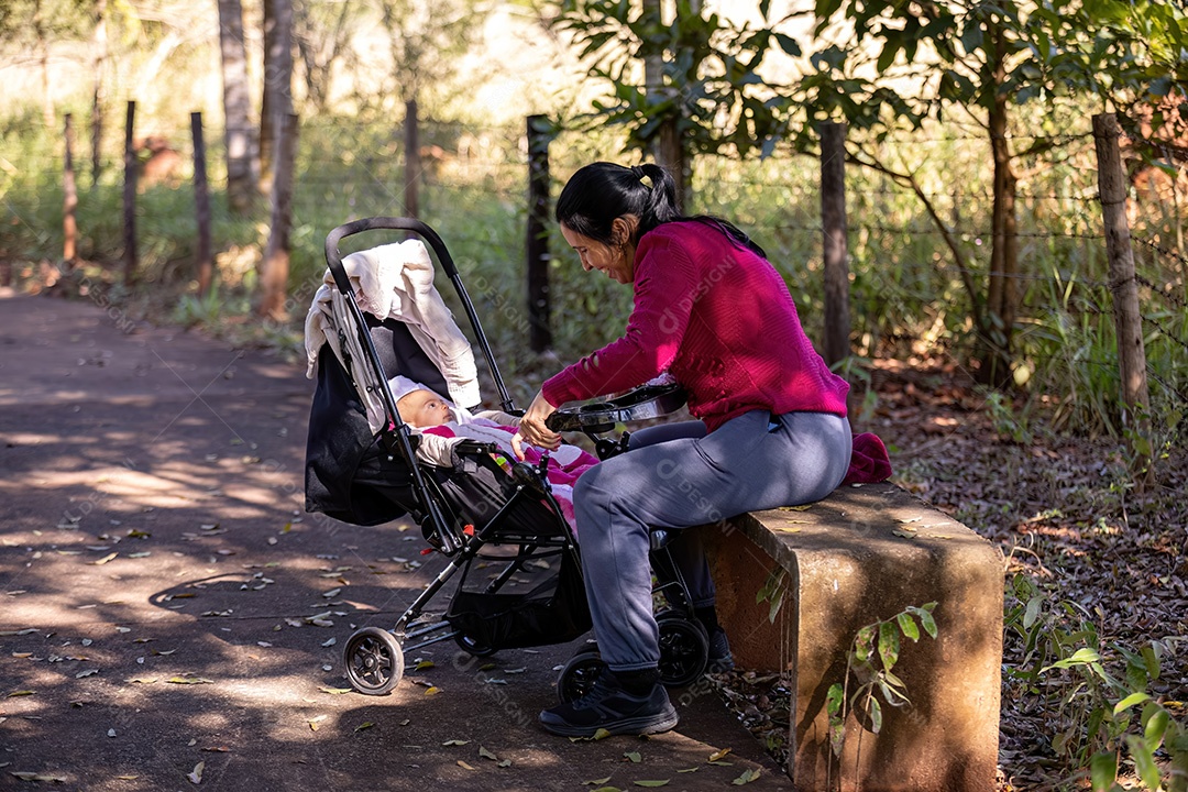 Mãe sentada no banco do parque interagindo com seu bebê no carrinho