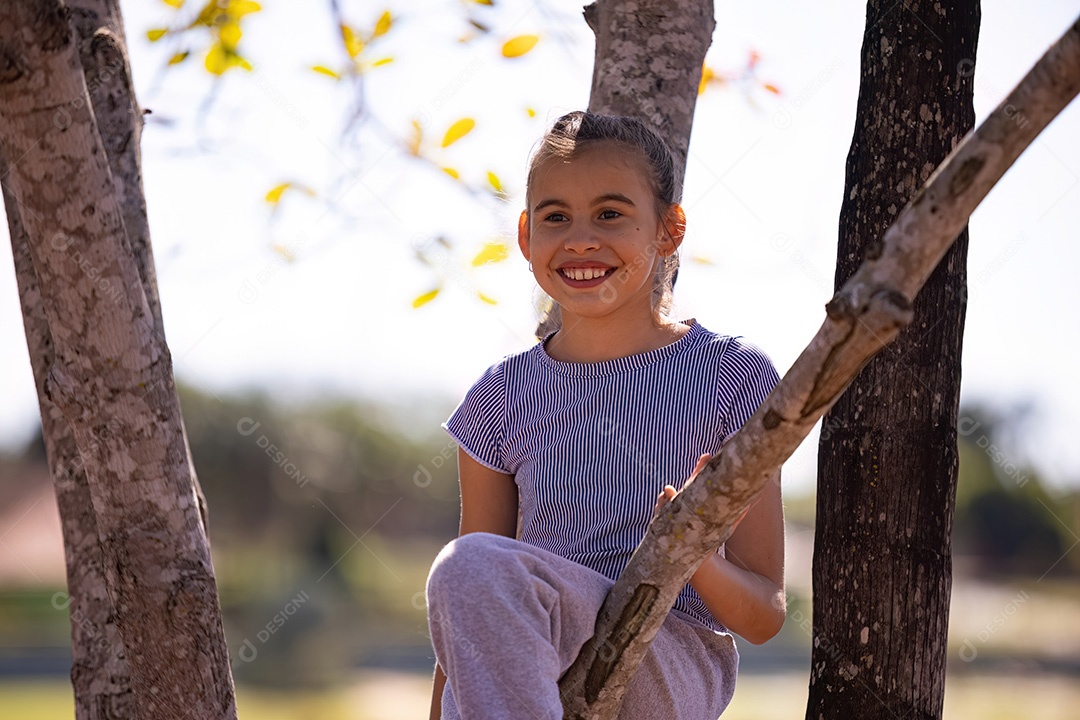 Uma menina com roupas cinza brincando em uma árvore em um parque com foco seletivo