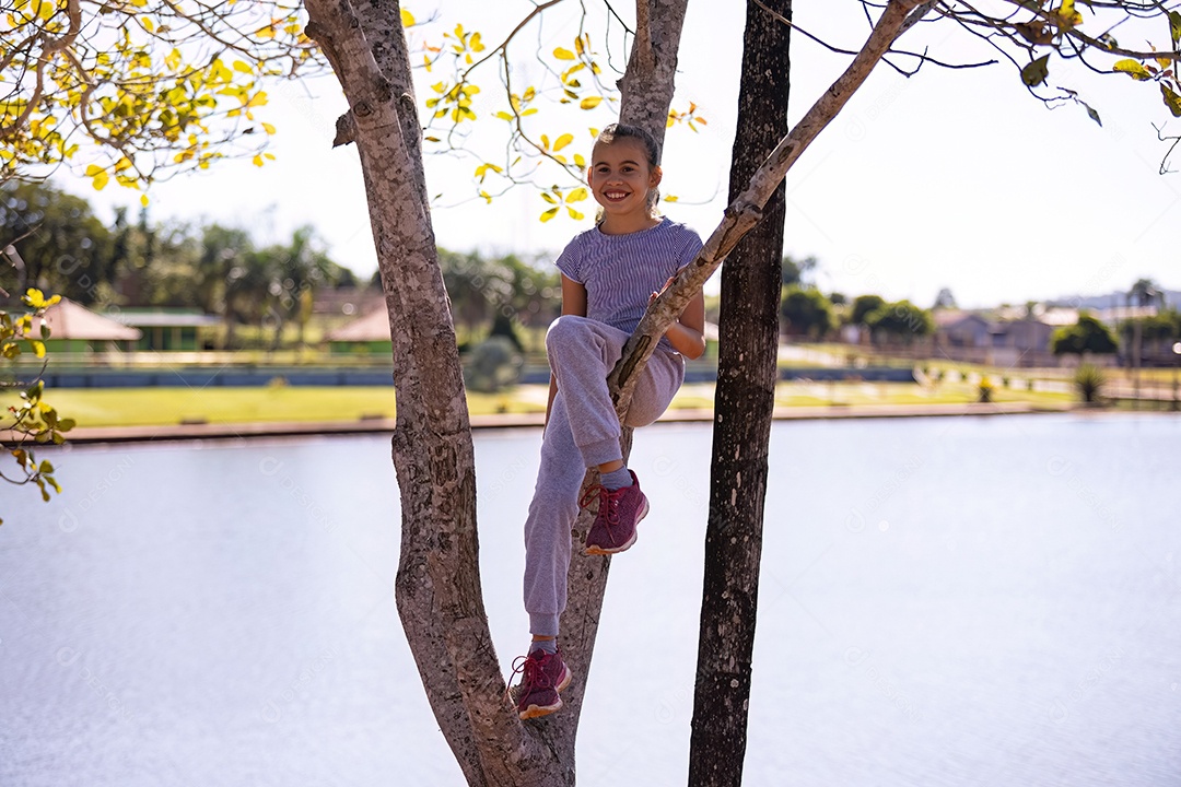 Uma menina com roupas cinza brincando em uma árvore em um parque com foco seletivo