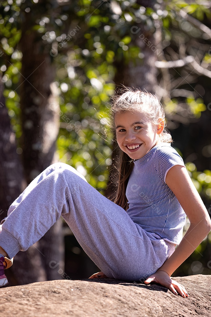 Uma menina com roupas cinza sorrindo feliz em uma pedra