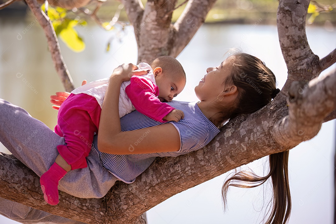 Uma menina com roupas cinza segurando uma criança recém-nascida com roupas brancas e rosa