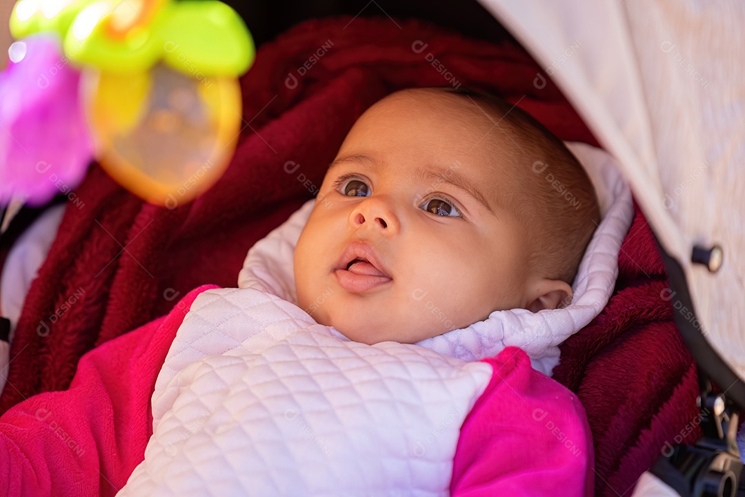 Rosto de uma menina recém-nascida com roupas brancas e rosa em um carrinho de bebê