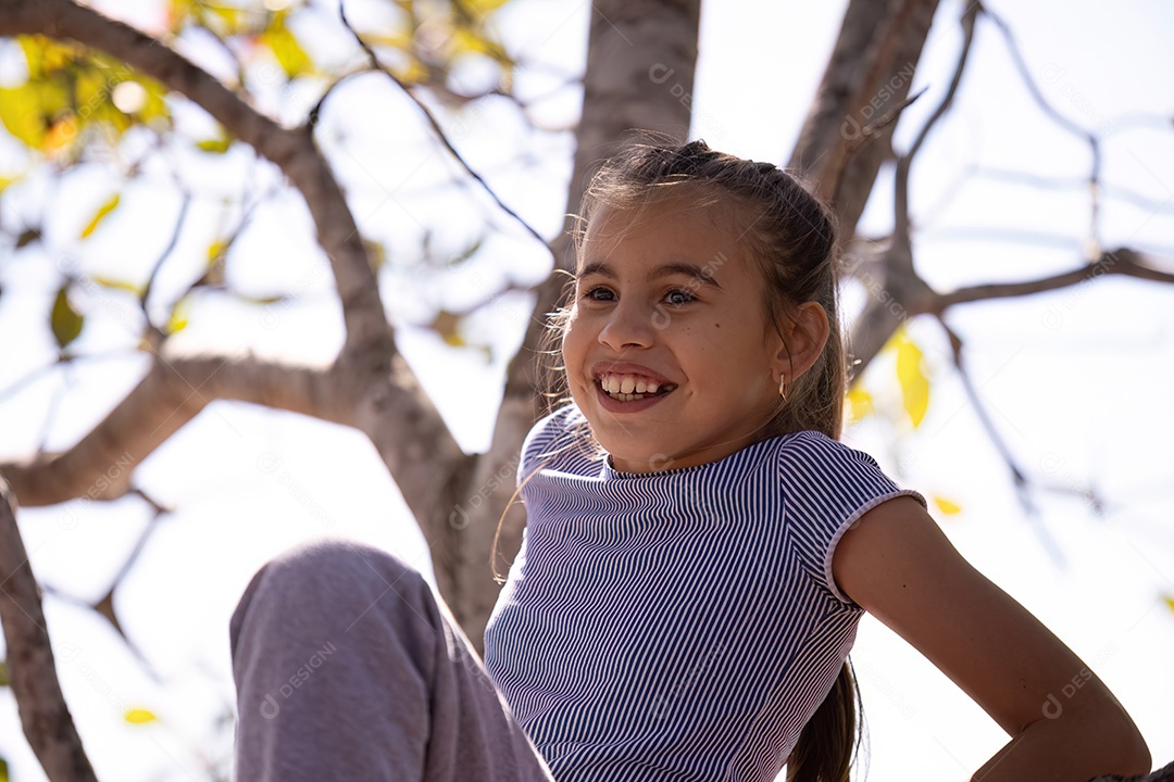 Uma menina com roupas cinza brincando em uma árvore em um parque com foco seletivo
