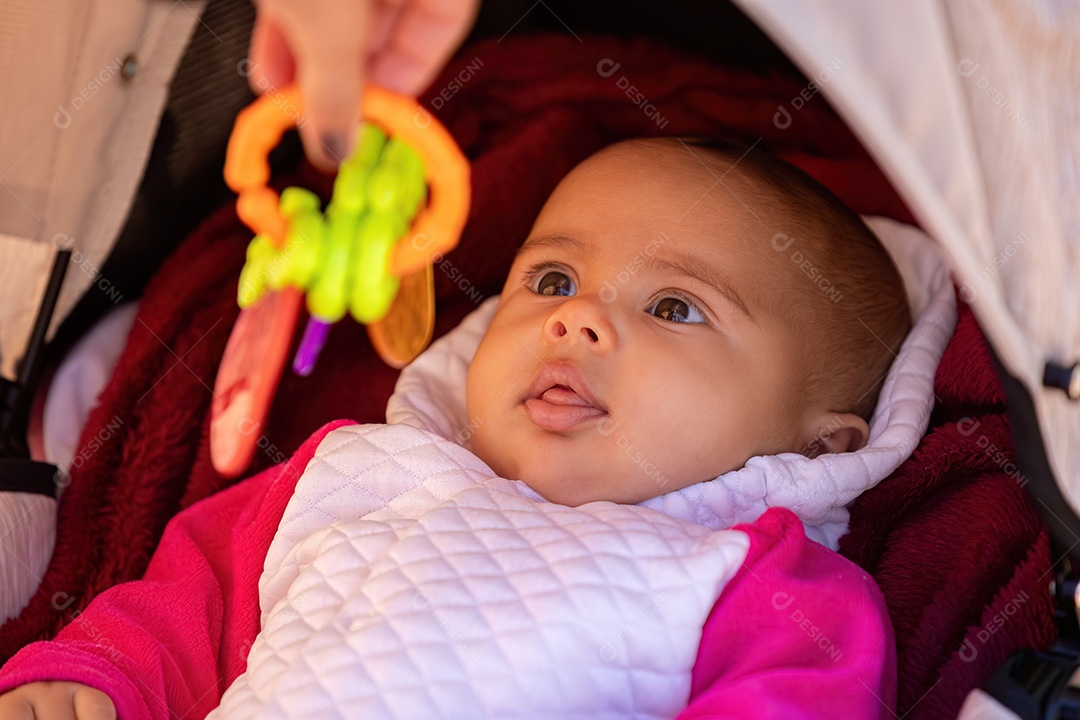 Rosto de uma menina recém-nascida com roupas brancas e rosa em um carrinho de bebê