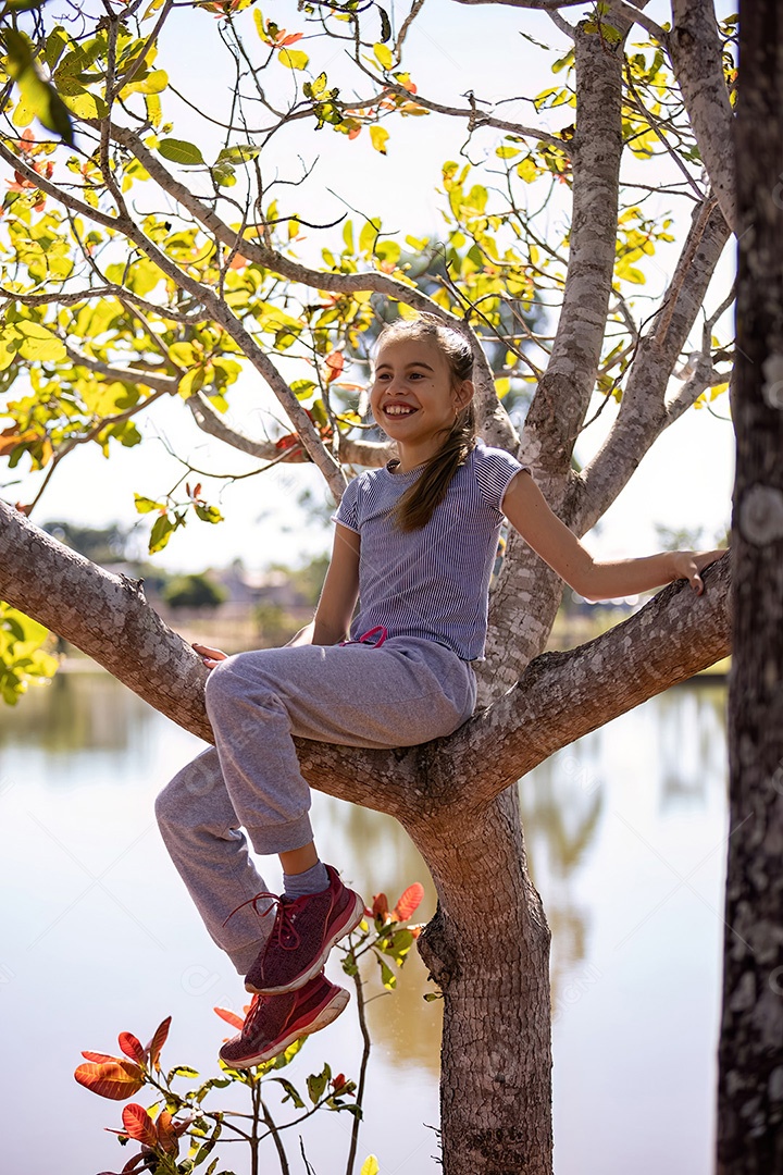 Uma menina com roupas cinza brincando em uma árvore em um parque com foco seletivo
