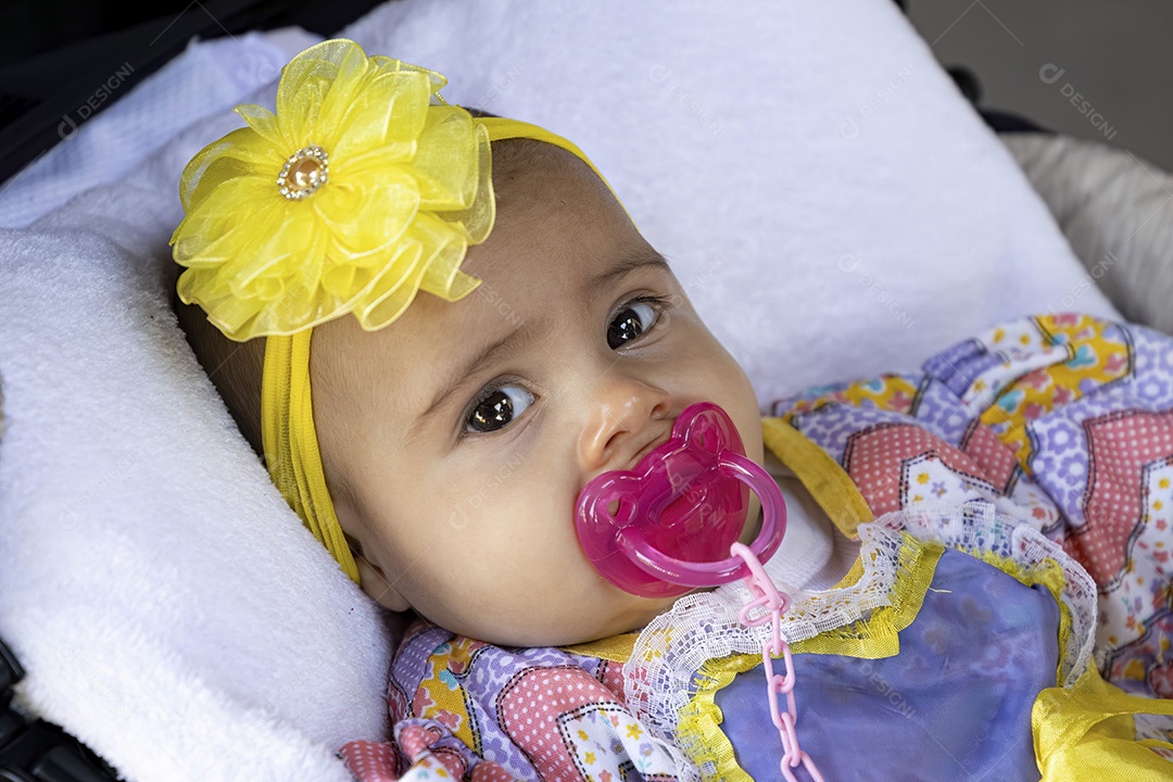 Menina recém-nascida no carrinho de bebê com roupas de festa e laço amarelo na cabeça