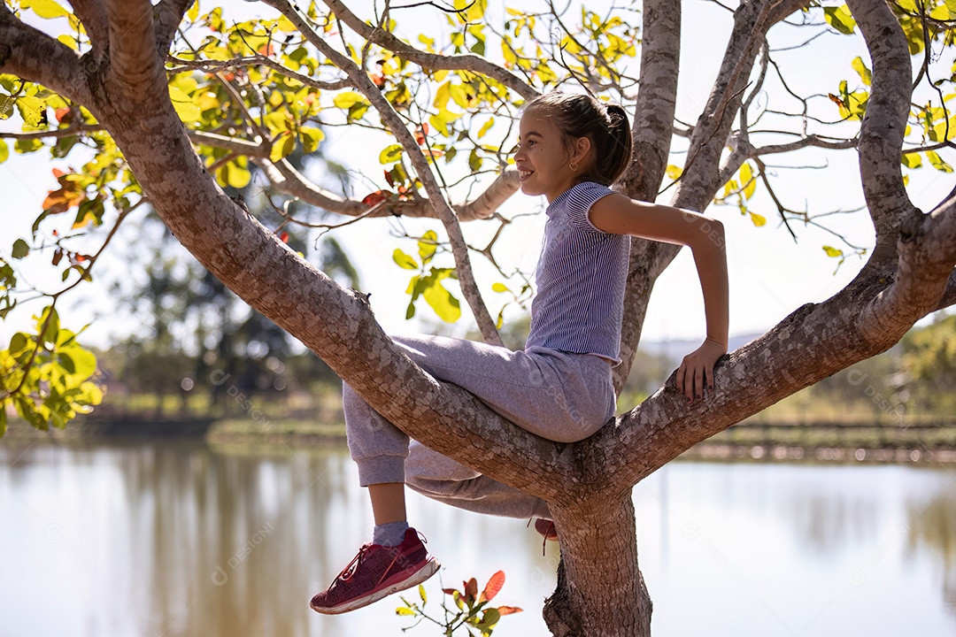 Uma menina com roupas cinza brincando em uma árvore em um parque com foco seletivo