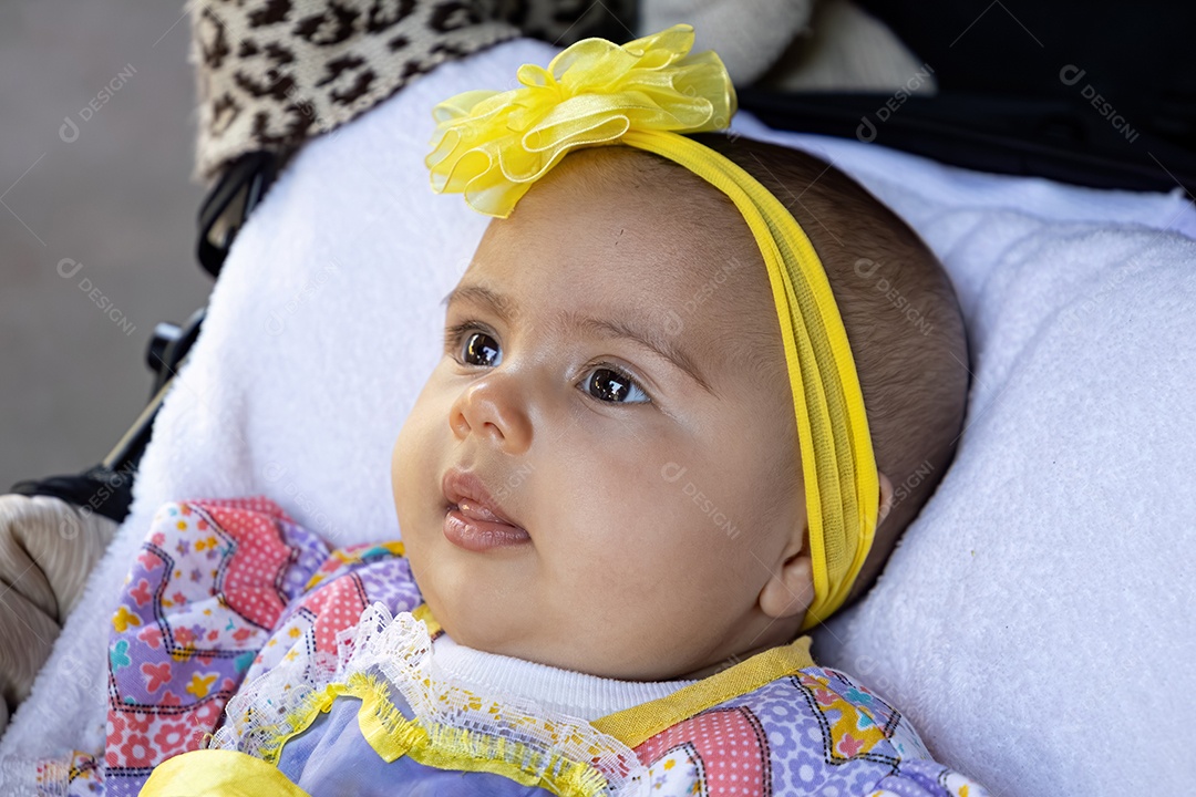 Menina recém-nascida no carrinho de bebê com roupas de festa e laço amarelo na cabeça
