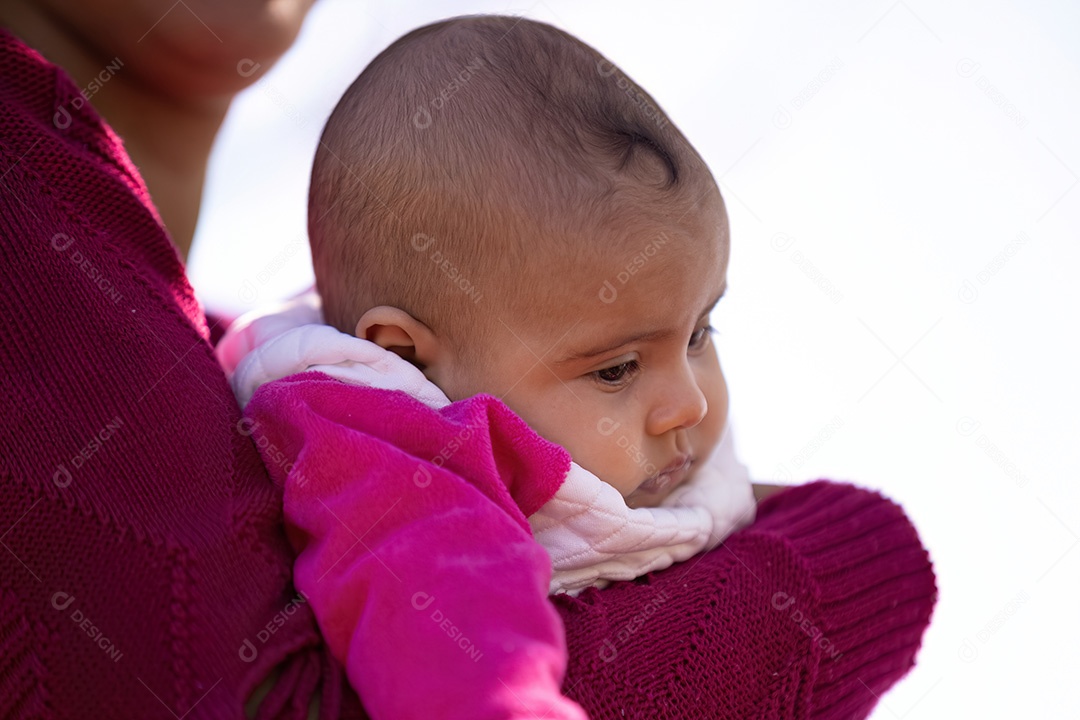 Rosto de uma menina com roupas cor de rosa segurada pela mãe