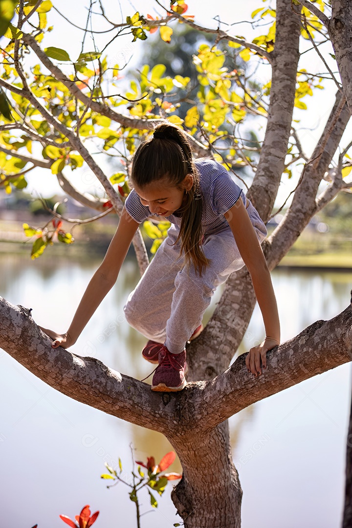 Uma menina com roupas cinza brincando em uma árvore em um parque com foco seletivo
