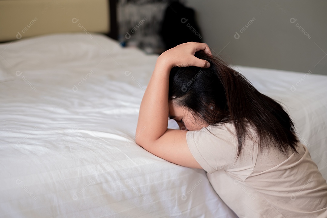 Triste mulher asiática deprimida sofrendo na cama branca, ela está sentada na cama e tocando a testa