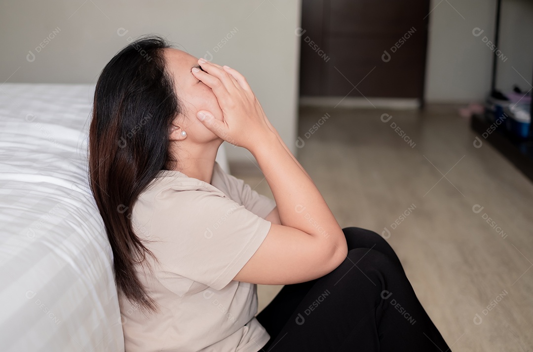 Triste mulher asiática deprimida sofrendo na cama branca, ela está sentada na cama e tocando a testa