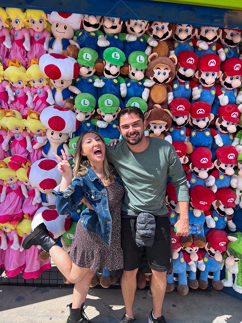 Casal feliz se divertindo com muitos bonecos de pelúcia atrás.