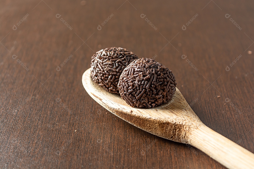 Brigadeiro brasileiro com chocolate granulado em uma colher de pau sobre a mesa de madeira.