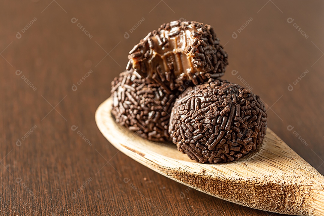 Brigadeiro brasileiro com chocolate granulado em uma colher de pau sobre a mesa de madeira.
