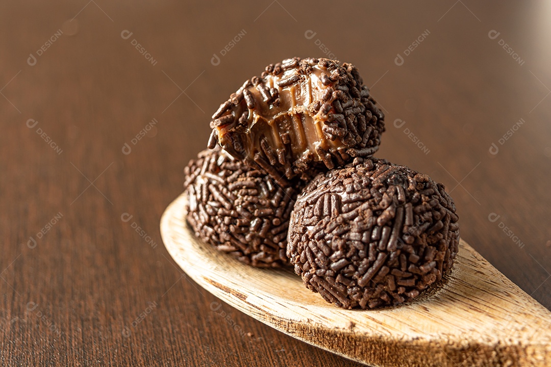 Brigadeiro brasileiro com chocolate granulado em uma colher de pau sobre a mesa de madeira.