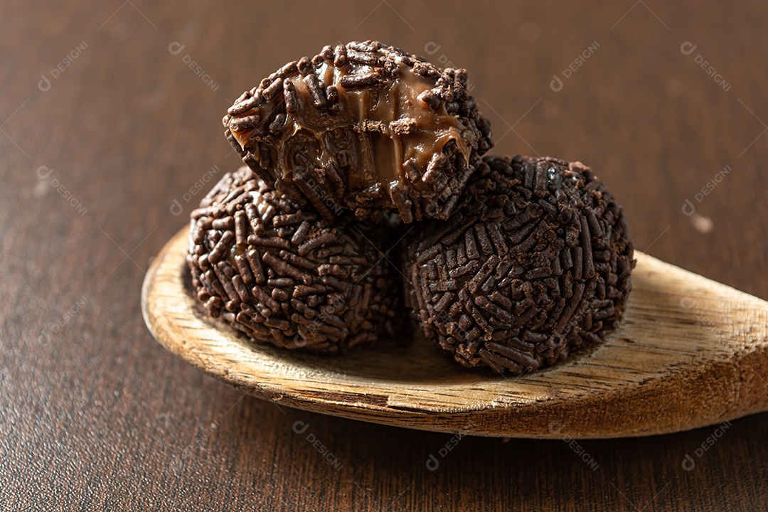 Brigadeiro brasileiro com chocolate granulado em uma colher de pau sobre a mesa de madeira.