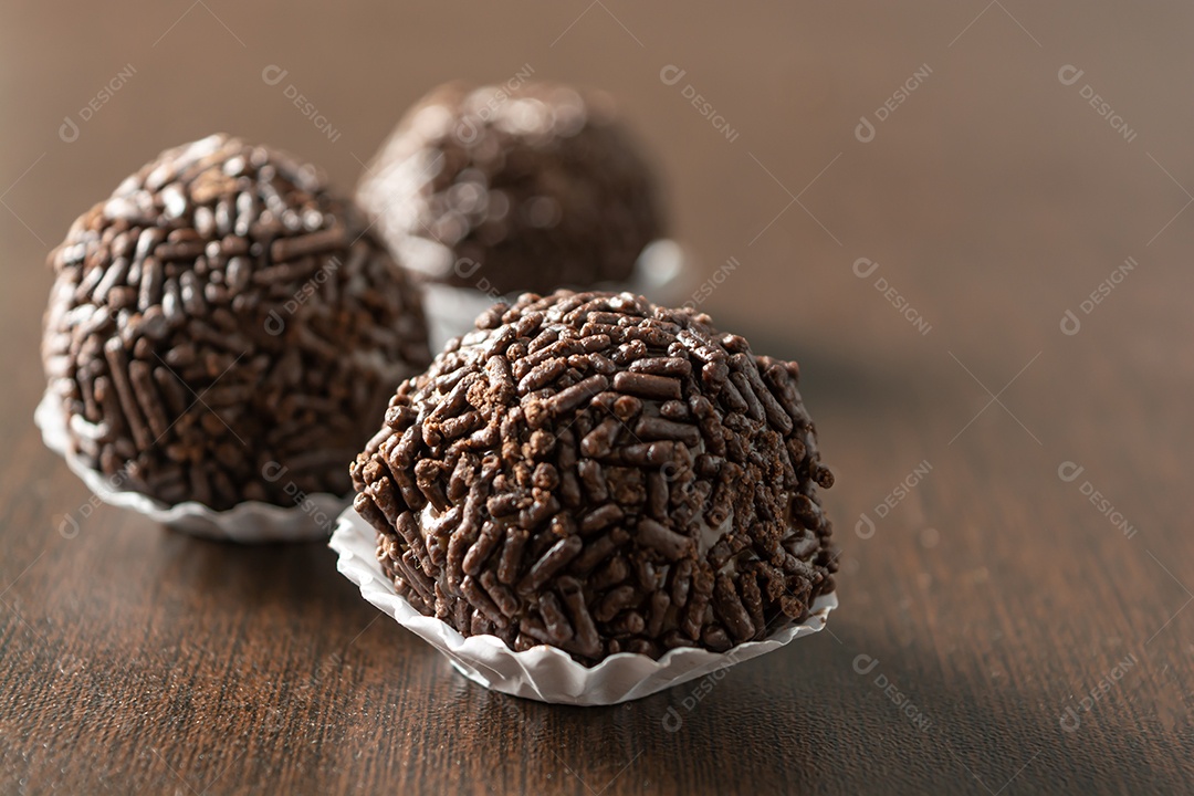 Brigadeiro brasileiro com chocolate granulado em uma colher de pau sobre a mesa de madeira.