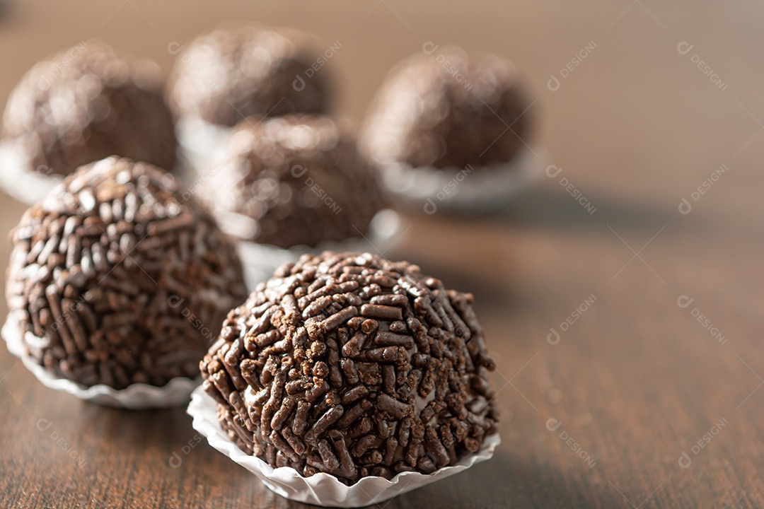 Brigadeiro brasileiro com chocolate granulado em uma colher de pau sobre a mesa de madeira.