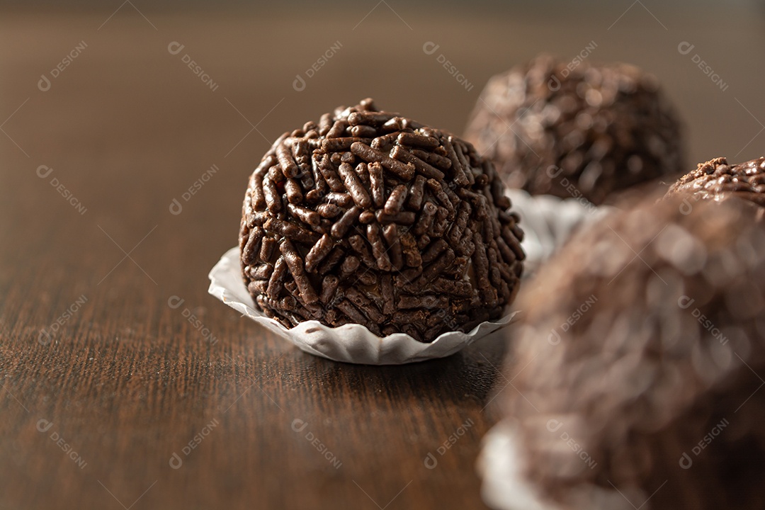 Brigadeiro brasileiro com chocolate granulado em uma colher de pau sobre a mesa de madeira.