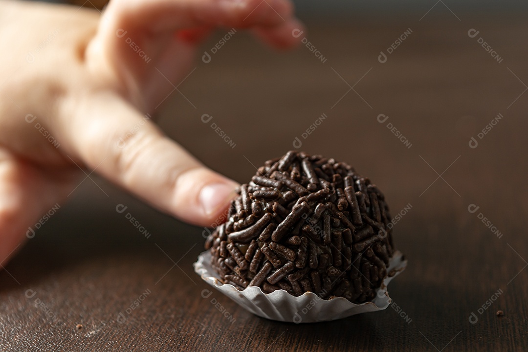 Brigadeiro brasileiro com chocolate granulado em uma colher de pau sobre a mesa de madeira.