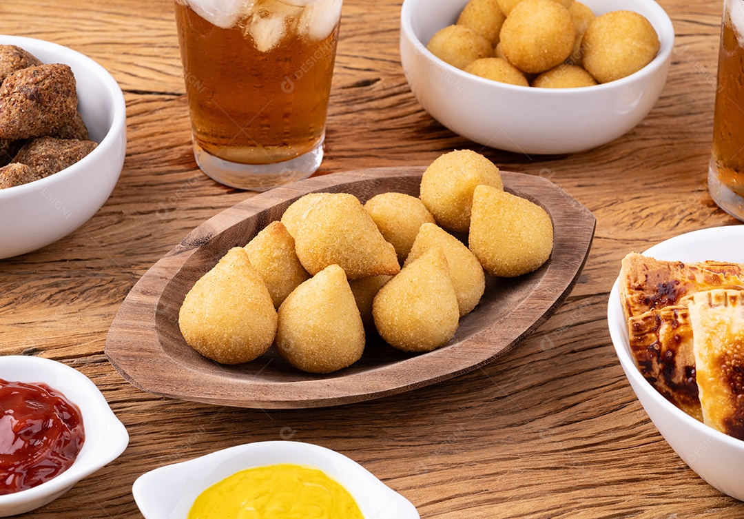 Coxinha de lanche típico brasileiro em prato com copo de refrigerante, ketchup e mostarda.