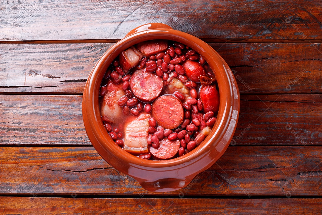 Feijoada brasileira em tigela de cerâmica isolada sobre fundo de madeira rústica.