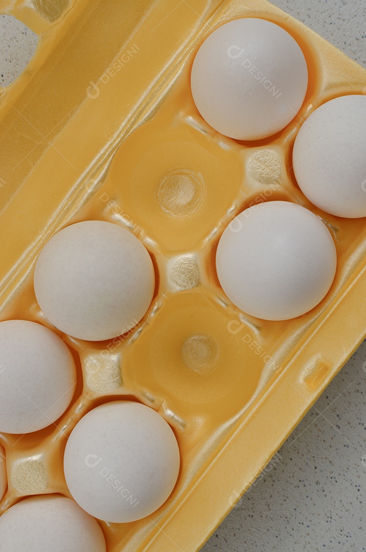 Ovos brancos cuidadosamente embalados em uma caixa amarela, prontos para uso culinário.