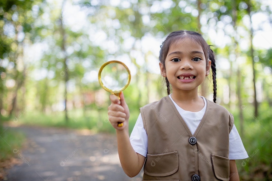 Uma garotinha asiática usando uma lupa para estudar um besouro-veado em um parque.