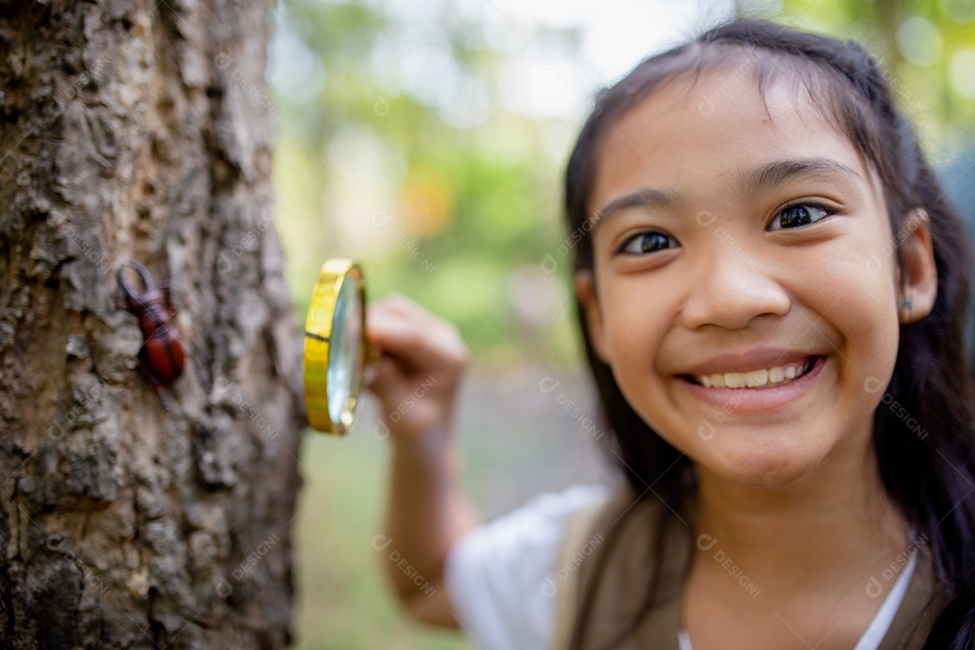 Uma garotinha asiática usando uma lupa para estudar um besouro-veado em um parque.