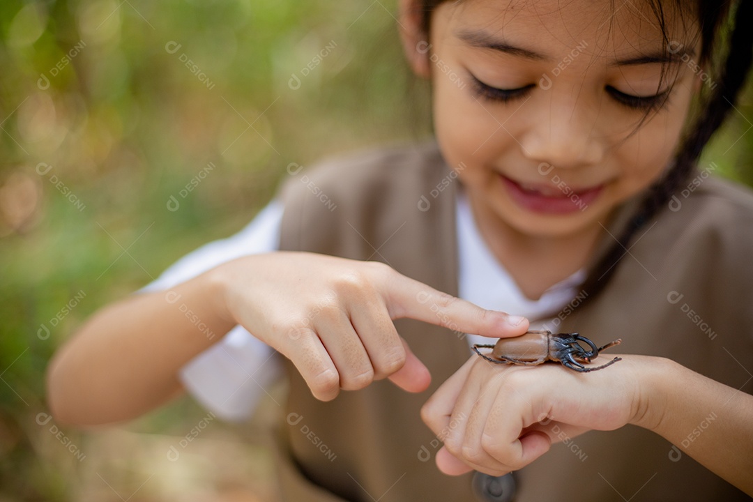 Uma garotinha asiática usando uma lupa para estudar um besouro-veado em um parque.