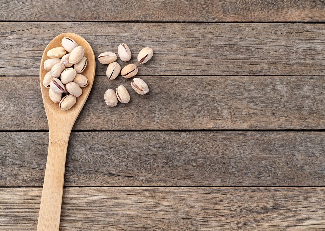 Pistácios torrados salgados em uma colher sobre a mesa de madeira com espaço de cópia.