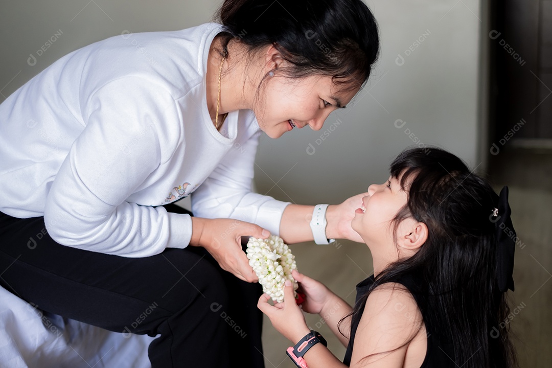 Dia das mães, linda garota asiática sorrindo e segurando uma guirlanda de flores para dar à mãe, conceito de calor familiar