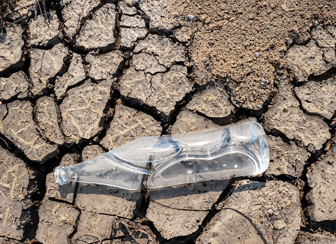 Garrafa de água cristalina em solo seco  e rachado